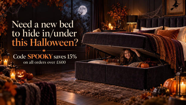 A dark upholstered storage bed with the lift-up lid open, showing a woman sitting underneath in a cozy Halloween-themed bedroom. The scene includes pumpkins, candles, autumn decor, and promotional text on the left offering a 15% code 'SPOOKY' on orders over £600.
