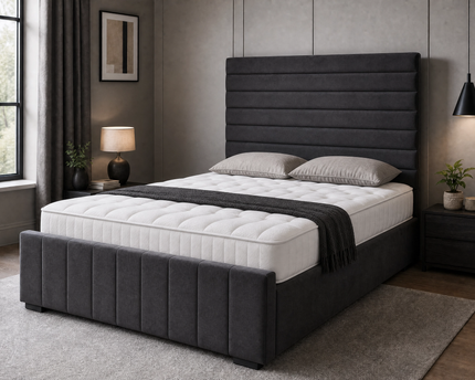 The Belmont Divan Ottoman Bed in charcoal grey velvet with horizontal pleated headboard and vertical panel footboard, shown closed with mattress and pillows in a modern bedroom setting, available in all UK sizes