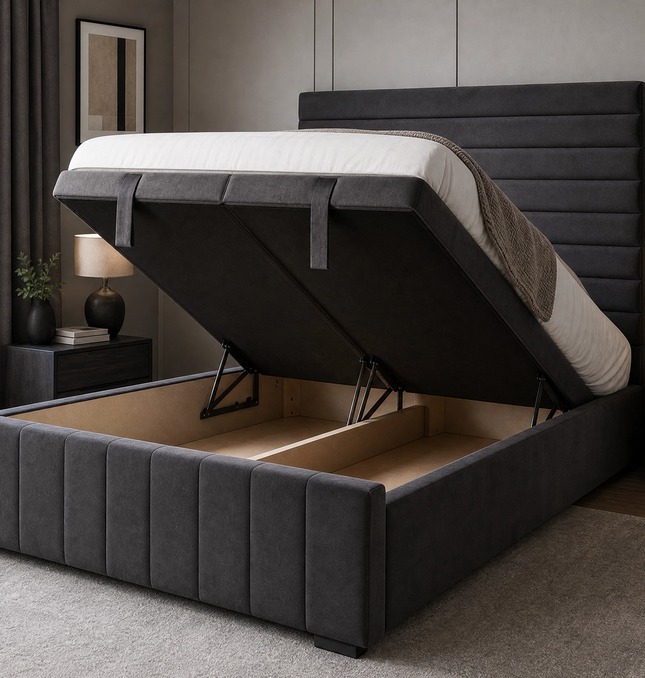 The Belmont Divan Ottoman Bed in charcoal grey velvet shown with end-lift storage mechanism open, revealing deep full-length storage cavity inside the upholstered divan base, featuring horizontal pleated headboard and vertical channel-stitched footboard